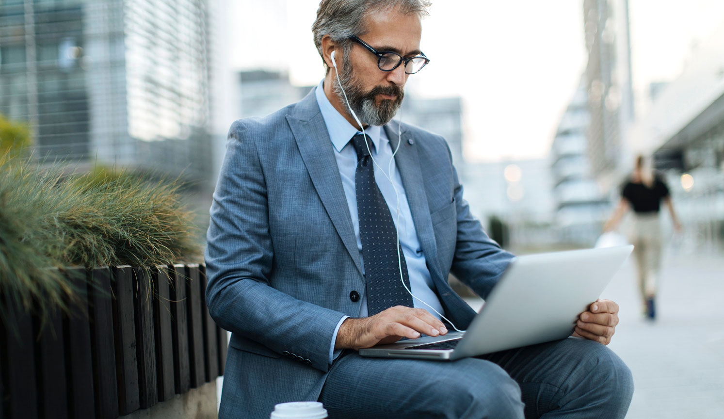 bearded businessman using laptop on lap outside, with earphones